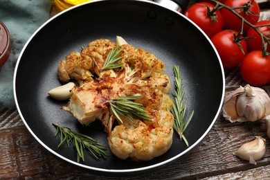 Photo of Tasty cauliflower steak in frying pan and other products on wooden table