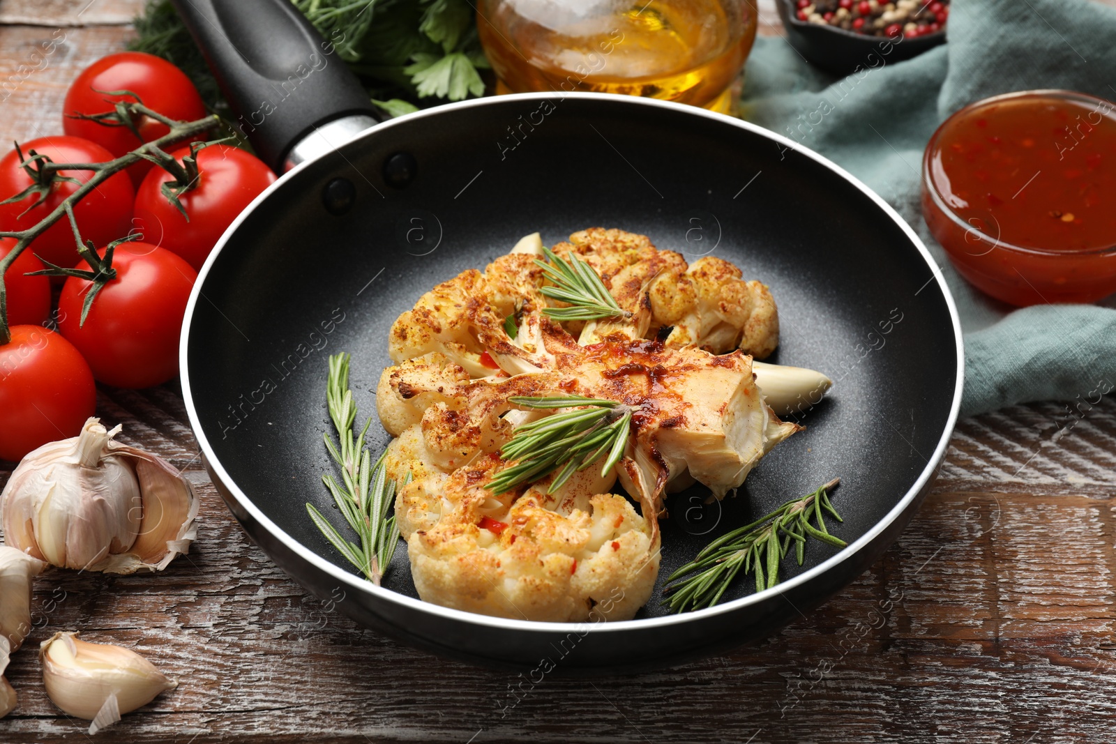 Photo of Tasty cauliflower steak in frying pan and other products on wooden table