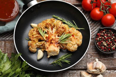 Photo of Tasty cauliflower steak in frying pan and other products on wooden table, top view