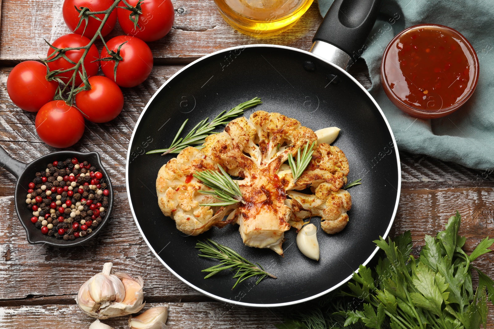 Photo of Tasty cauliflower steak in frying pan and other products on wooden table, top view