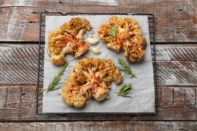 Photo of Tasty cauliflower steaks, rosemary and garlic on wooden table, top view