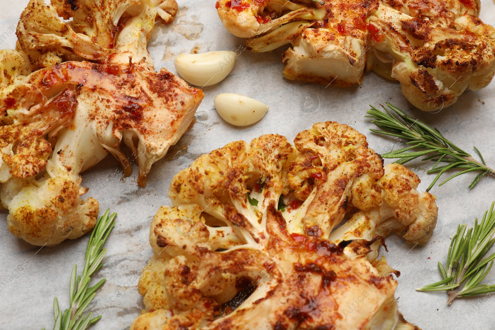 Photo of Tasty cauliflower steaks, rosemary and garlic on parchment paper, closeup