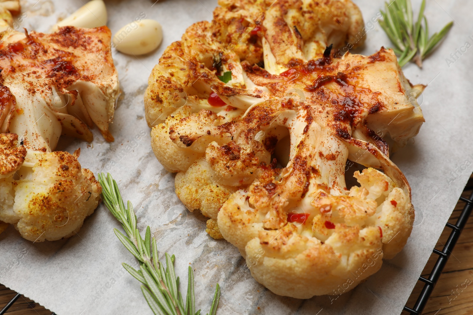 Photo of Tasty cauliflower steaks, rosemary and garlic on table, closeup