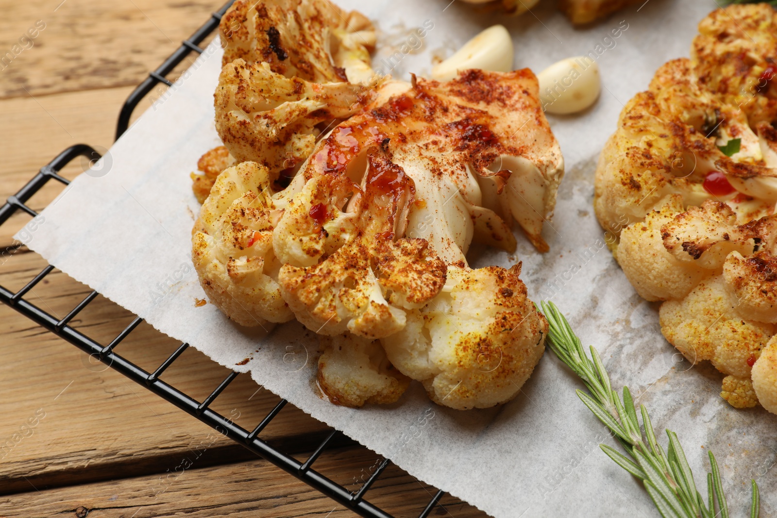 Photo of Tasty cauliflower steaks, rosemary and garlic on wooden table, closeup