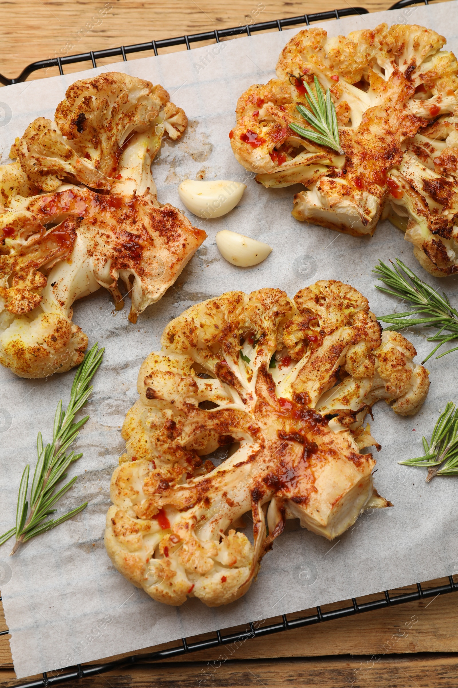 Photo of Tasty cauliflower steaks, rosemary and garlic on wooden table, top view