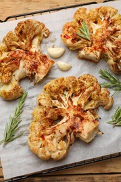 Photo of Tasty cauliflower steaks, rosemary and garlic on wooden table, top view