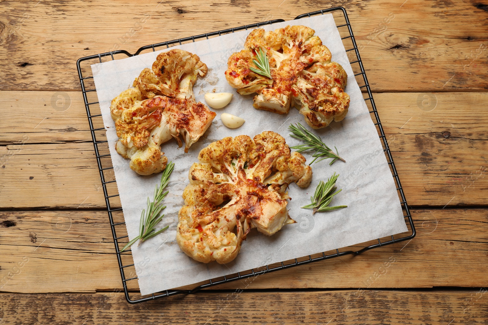 Photo of Tasty cauliflower steaks, rosemary and garlic on wooden table, top view