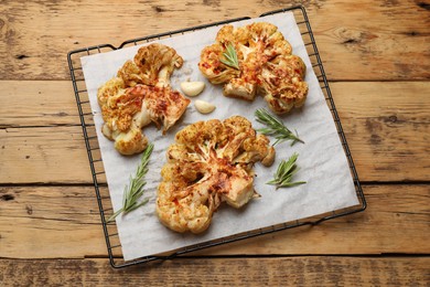 Photo of Tasty cauliflower steaks, rosemary and garlic on wooden table, top view