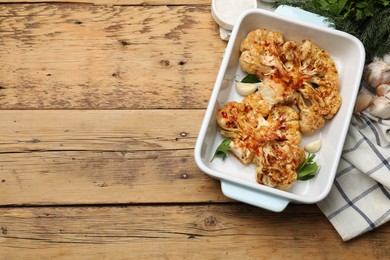 Photo of Tasty cauliflower steaks in baking dish and spices on wooden table, top view. Space for text