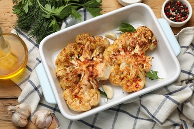 Photo of Tasty cauliflower steaks in baking dish and spices on wooden table, top view