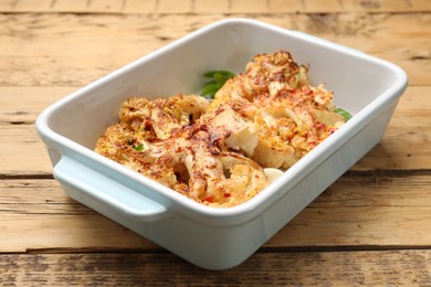 Photo of Tasty cauliflower steaks in baking dish and spices on wooden table, closeup