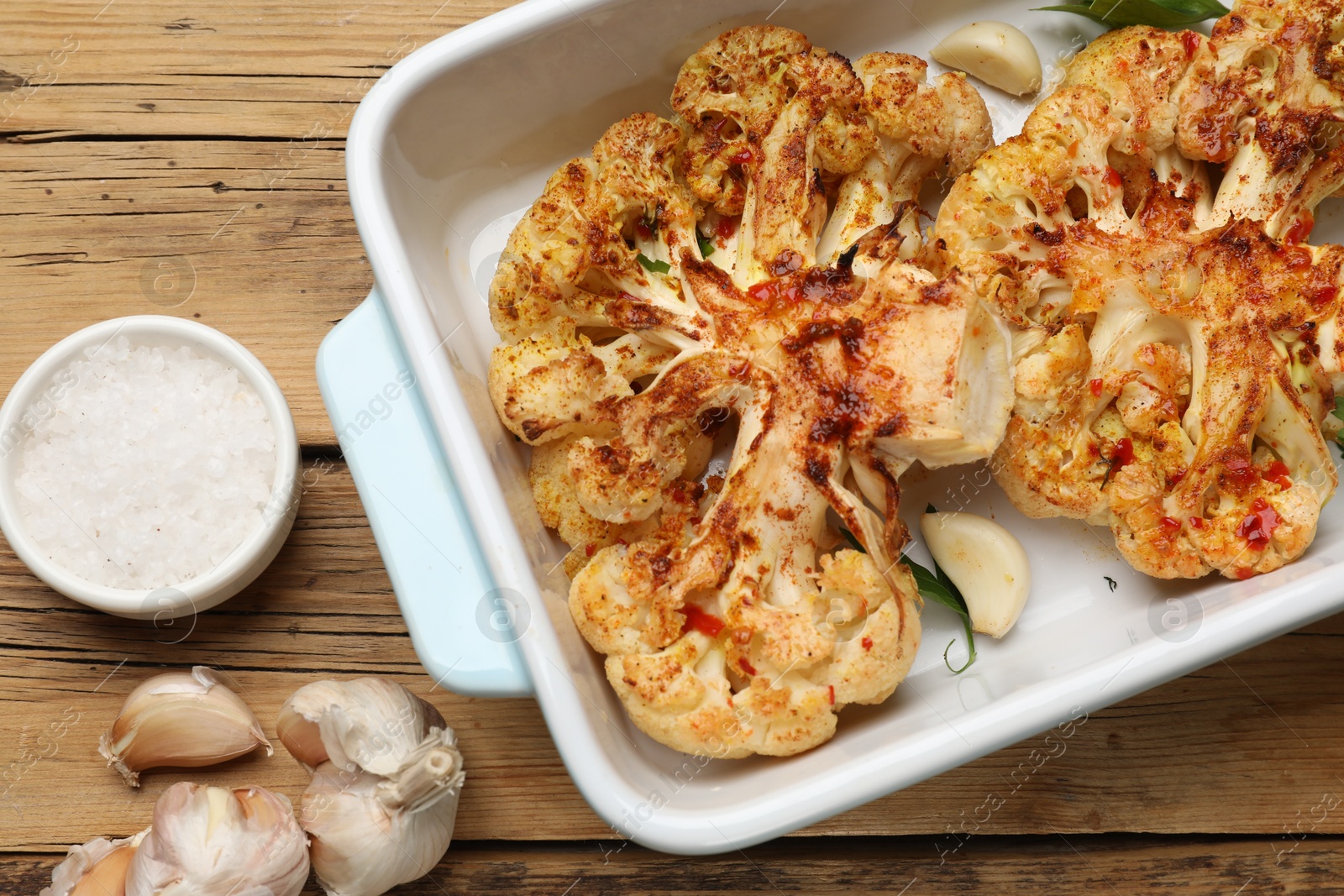 Photo of Tasty cauliflower steaks in baking dish and spices on wooden table, top view