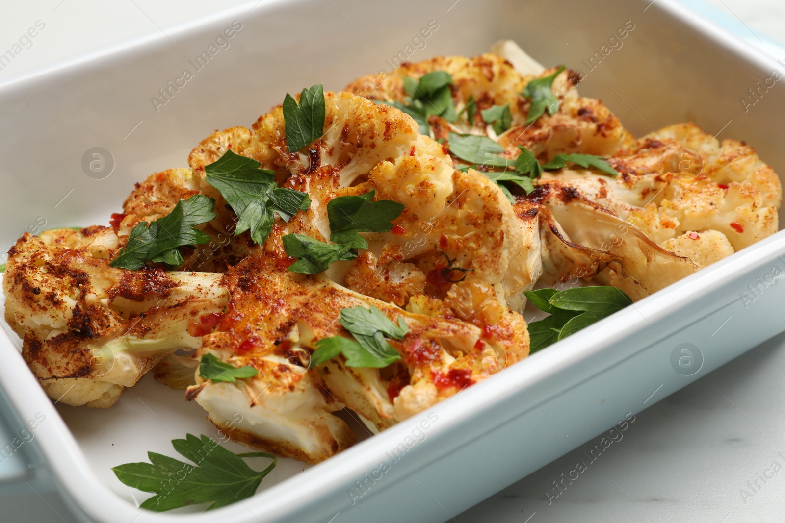 Photo of Tasty cauliflower steaks and parsley in baking dish on white table, closeup