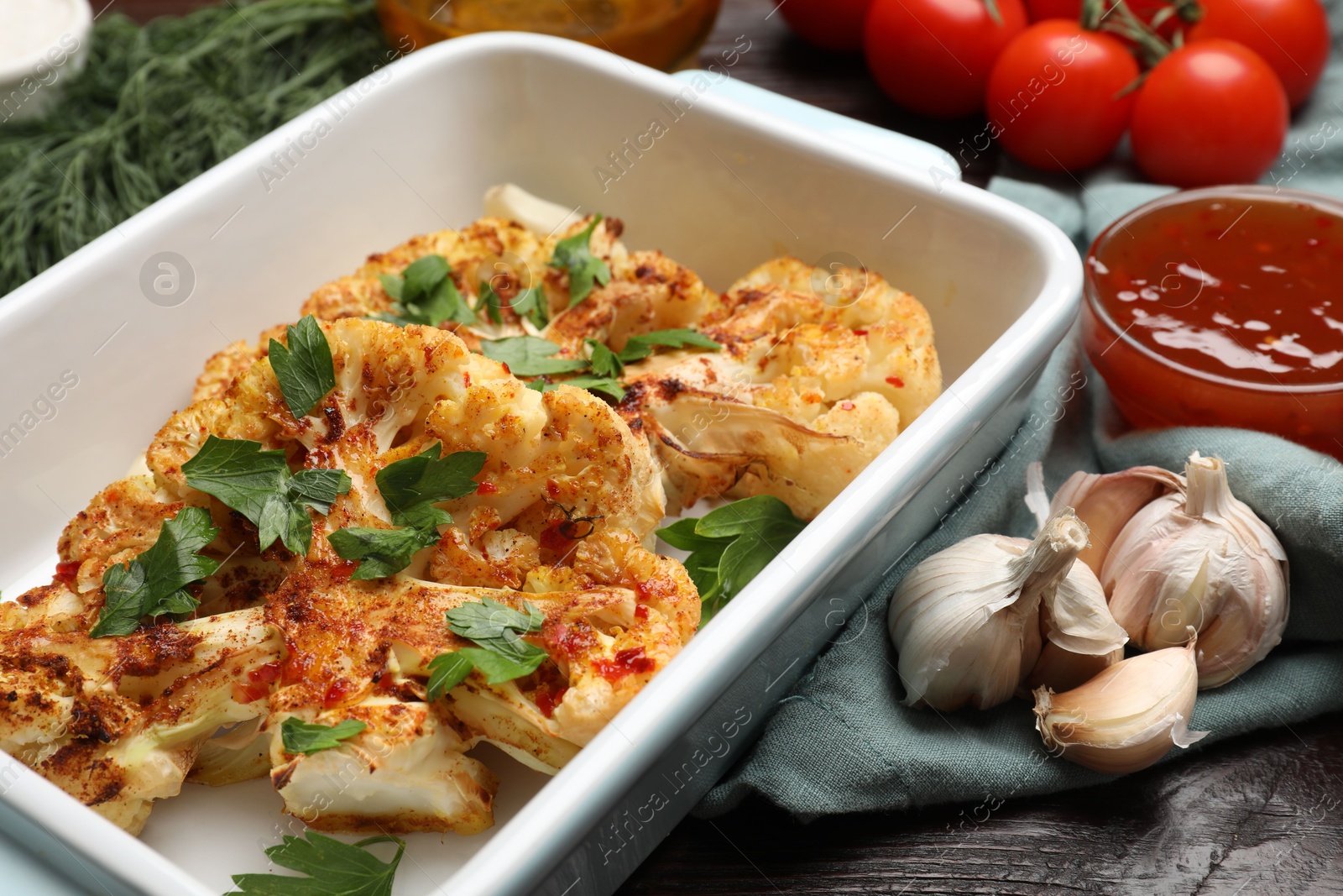 Photo of Tasty cauliflower steaks in baking dish and other products on wooden table, closeup