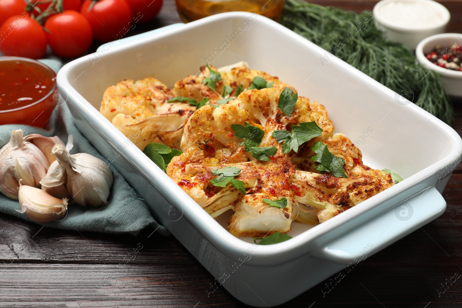 Photo of Tasty cauliflower steaks in baking dish and other products on wooden table, closeup