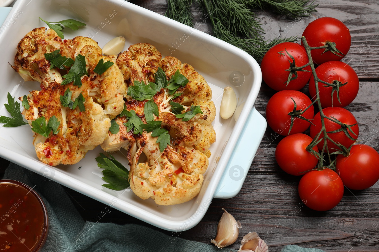 Photo of Tasty cauliflower steaks in baking dish and other products on wooden table, top view