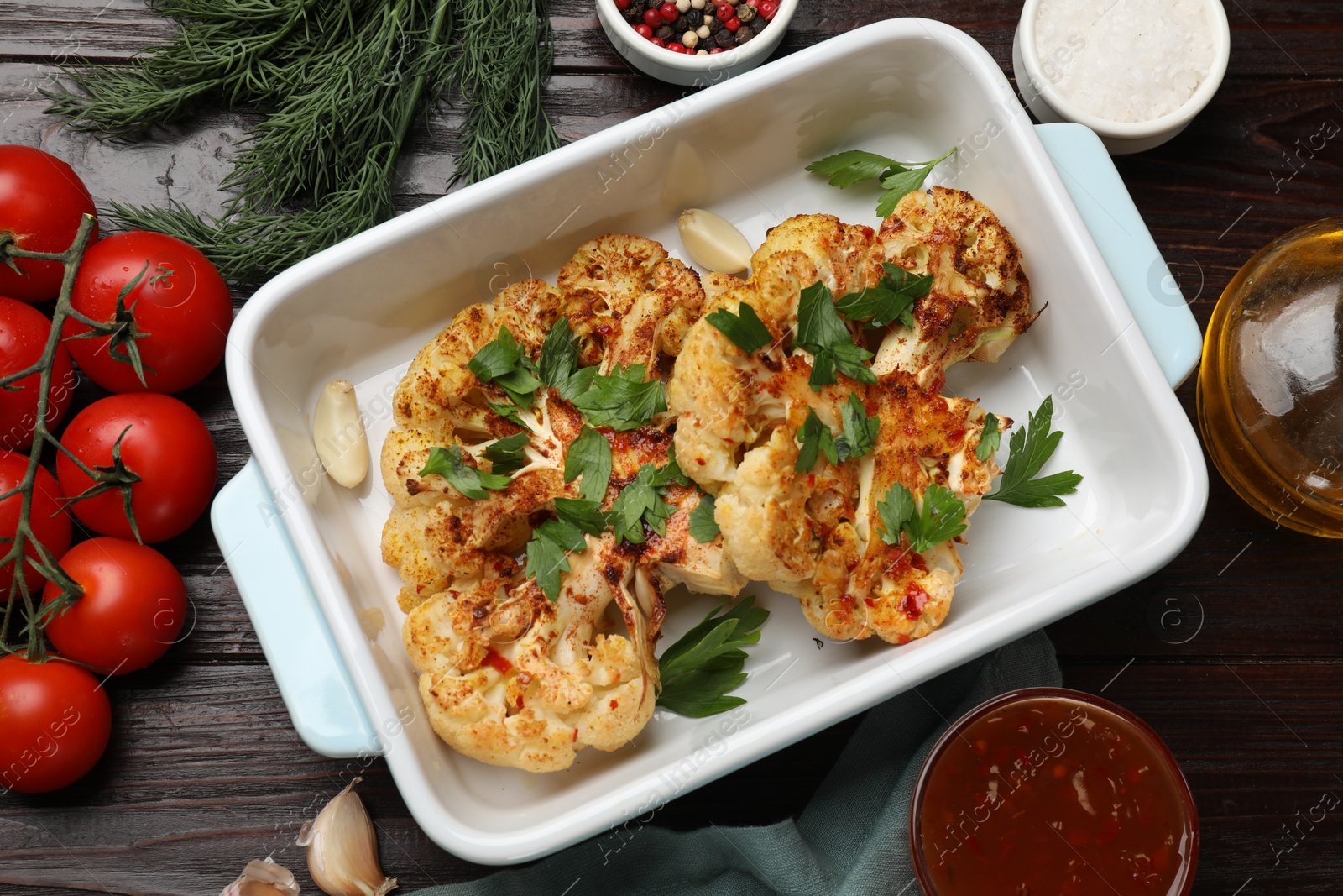 Photo of Tasty cauliflower steaks in baking dish and other products on wooden table, top view