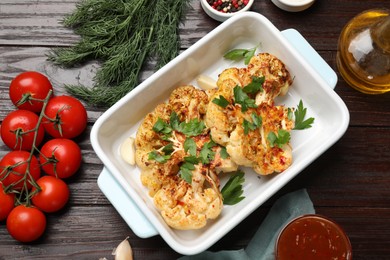 Photo of Tasty cauliflower steaks in baking dish and other products on wooden table, top view