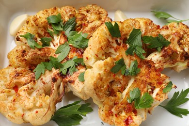 Photo of Tasty cauliflower steaks and parsley in baking dish, closeup