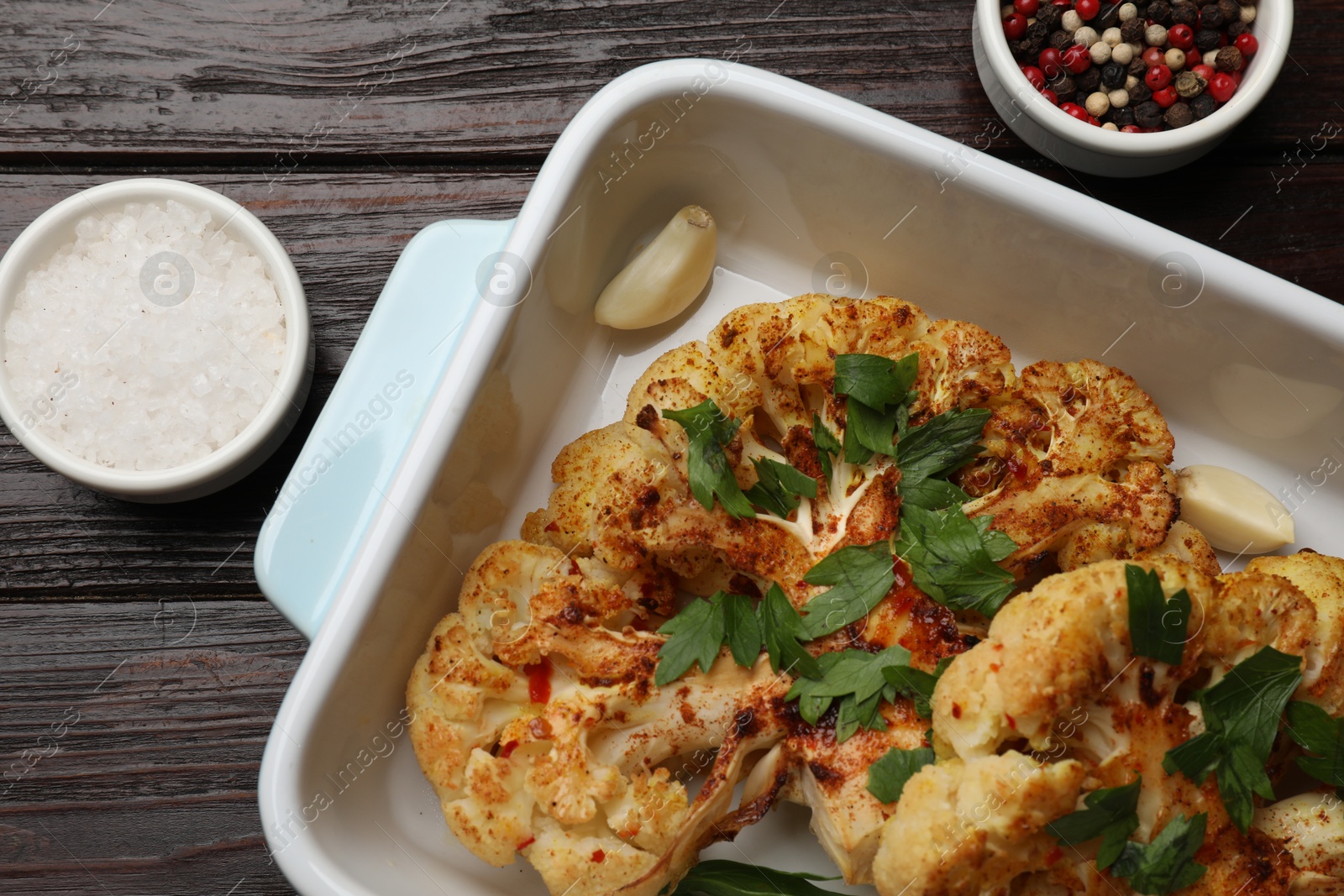 Photo of Tasty cauliflower steaks in baking dish and spices on wooden table, top view