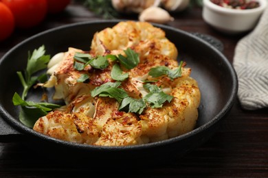 Photo of Tasty cauliflower steak and parsley in frying pan on wooden table, closeup