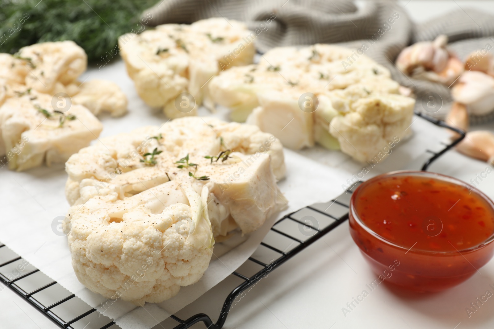 Photo of Uncooked cauliflower steaks and sauce on white table, closeup