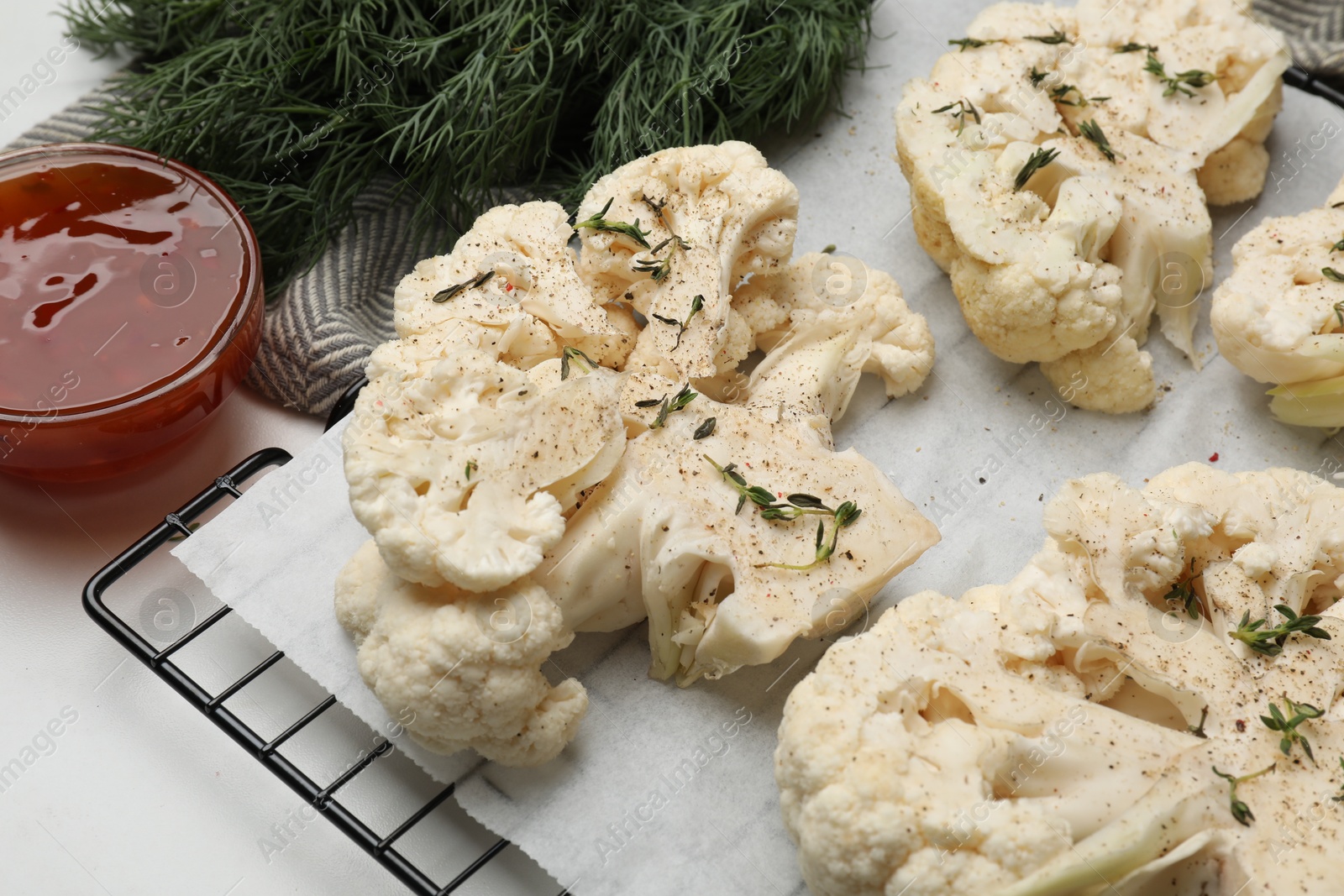 Photo of Uncooked cauliflower steaks, dill and sauce on white table, closeup