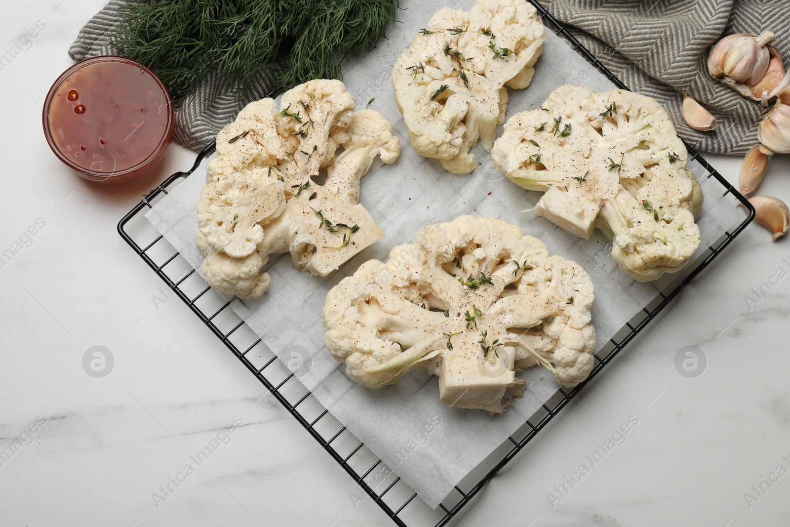 Photo of Uncooked cauliflower steaks, dill, garlic and sauce on white marble table, top view