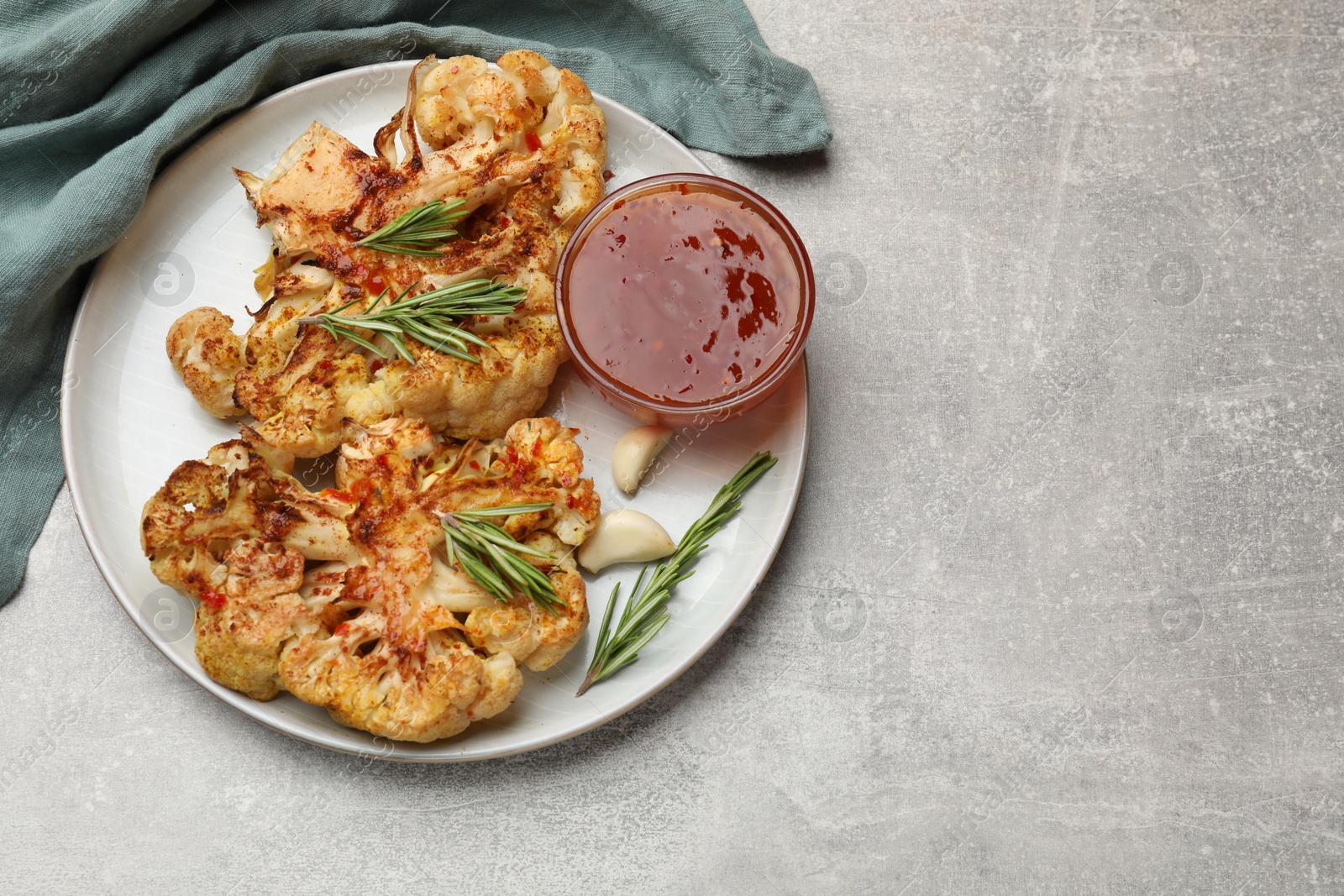 Photo of Delicious baked cauliflower steaks with sauce on grey table, top view. Space for text