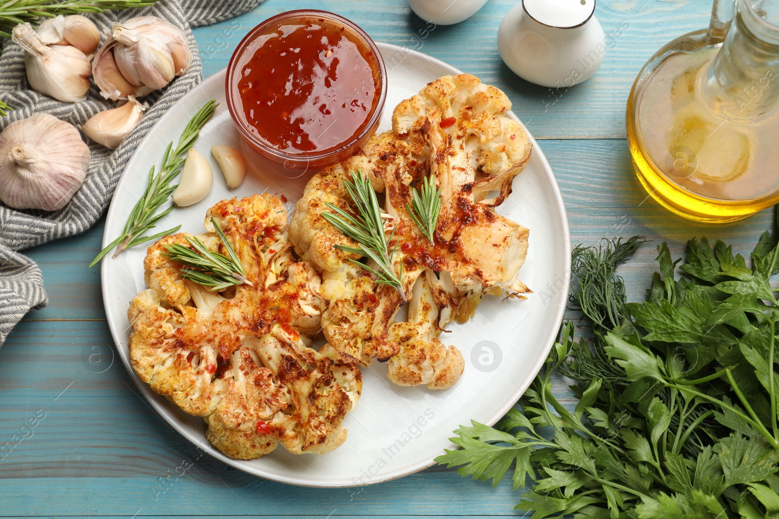 Photo of Delicious baked cauliflower steaks with sauce served on blue wooden table, flat lay