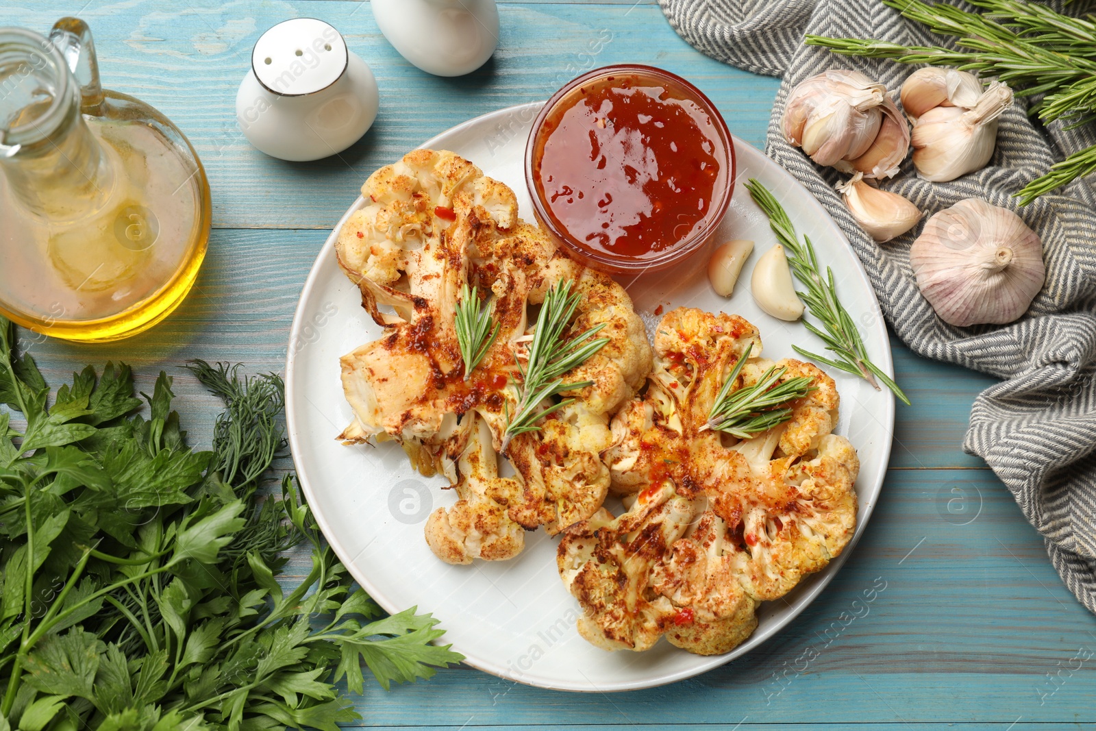 Photo of Delicious baked cauliflower steaks with sauce served on blue wooden table, flat lay