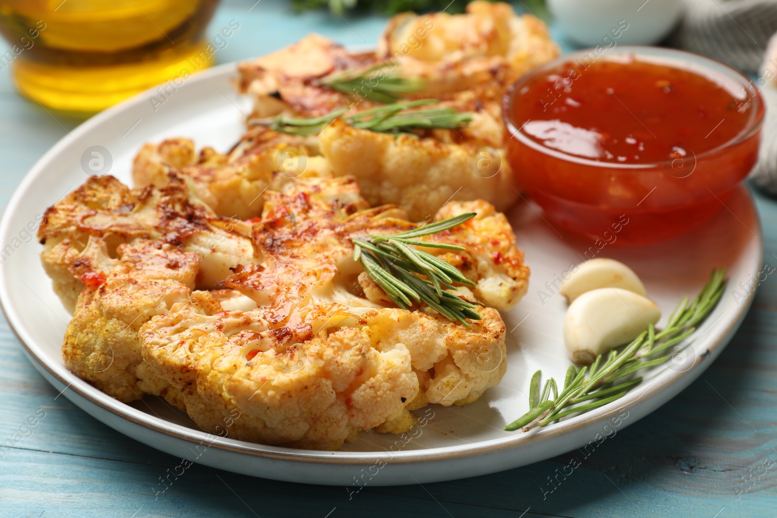 Photo of Delicious baked cauliflower steaks with sauce on blue wooden table, closeup