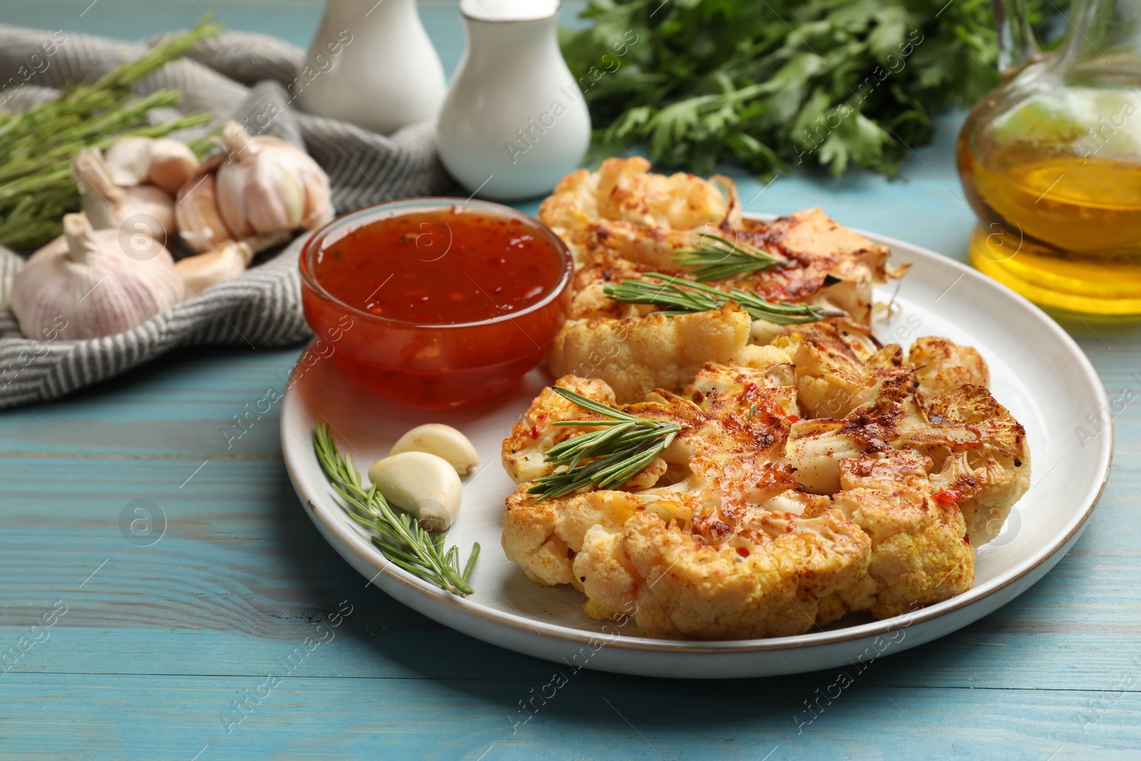 Photo of Delicious baked cauliflower steaks with sauce on blue wooden table