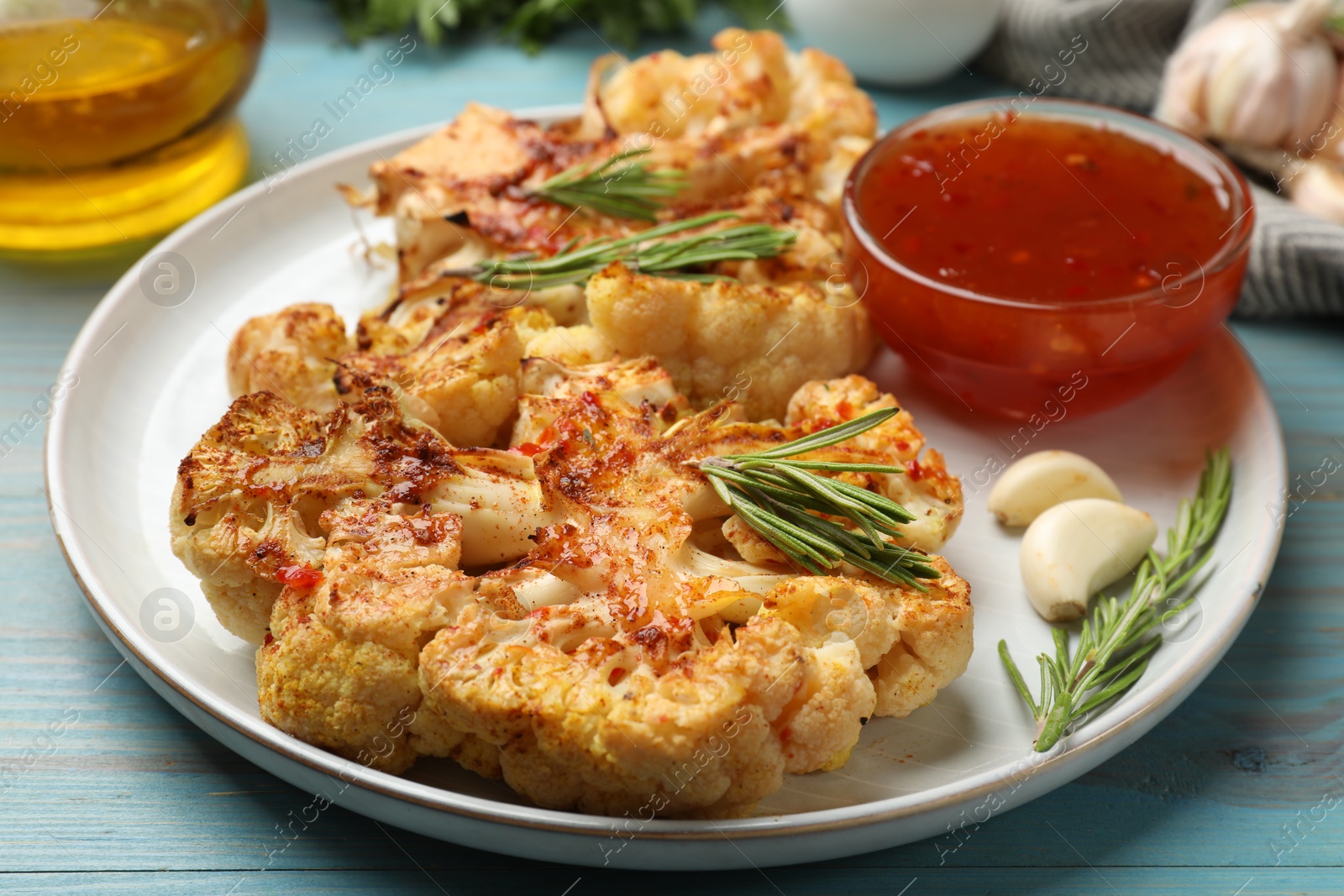 Photo of Delicious baked cauliflower steaks with sauce on blue wooden table, closeup