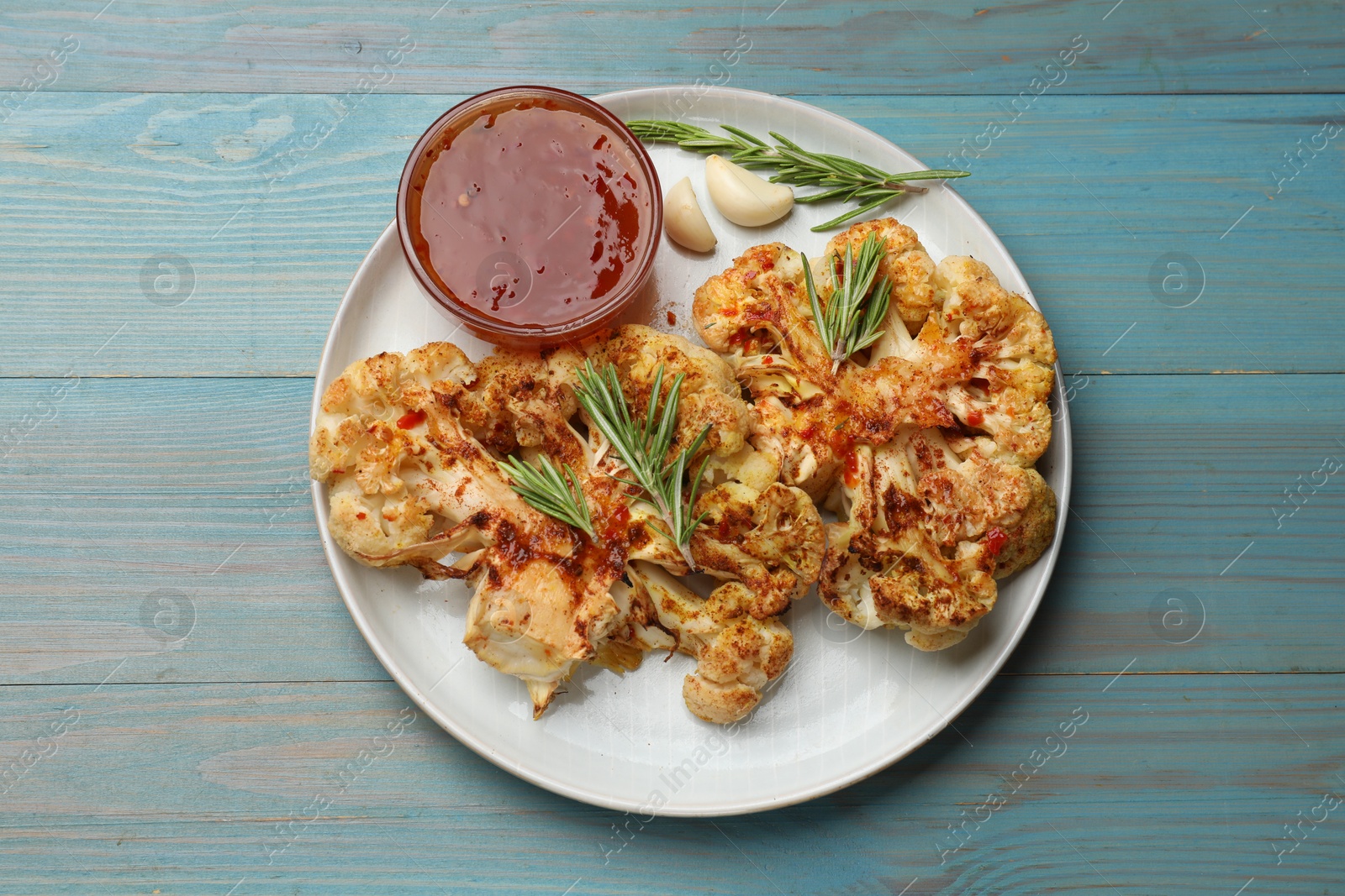 Photo of Delicious baked cauliflower steaks with sauce on blue wooden table, top view