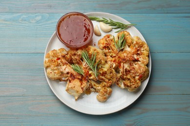 Delicious baked cauliflower steaks with sauce on blue wooden table, top view