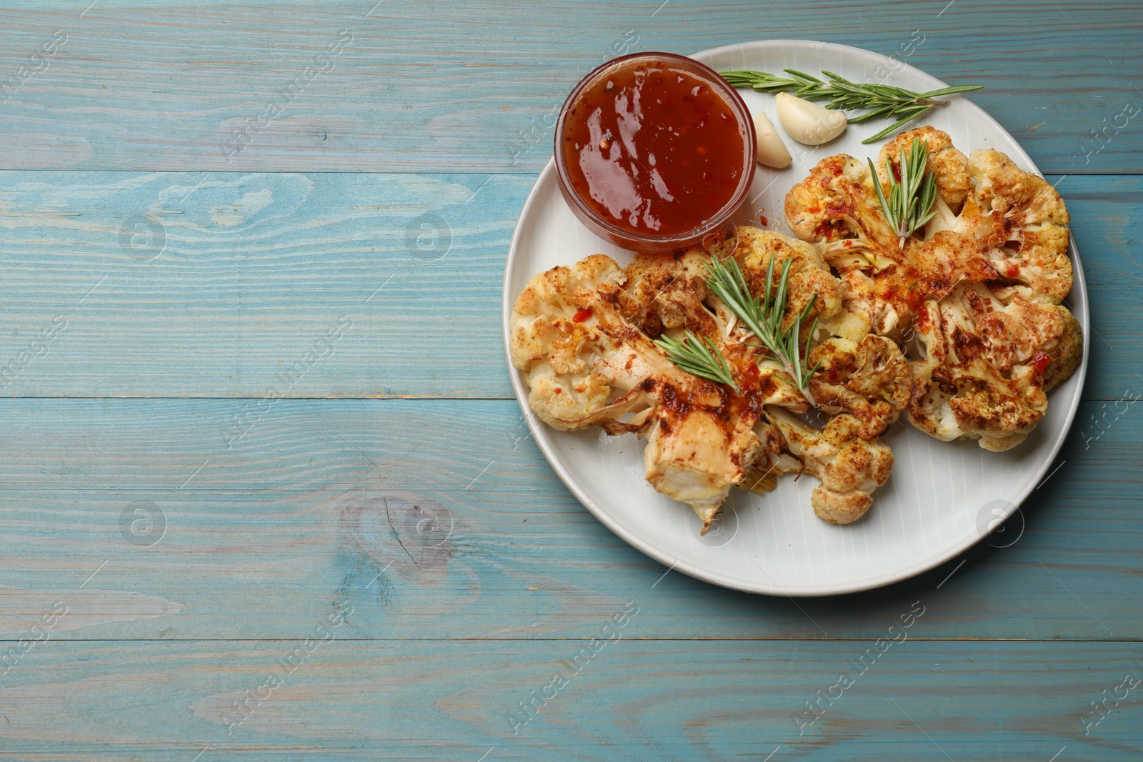 Photo of Delicious baked cauliflower steaks with sauce on blue wooden table, top view. Space for text