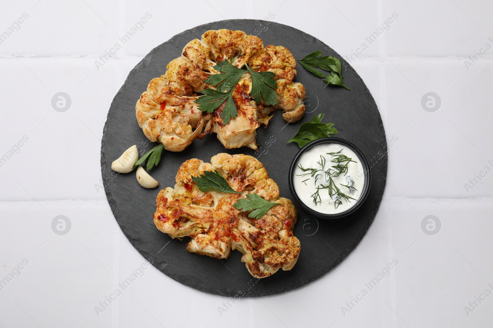 Photo of Delicious baked cauliflower steaks served on white tiled table, top view