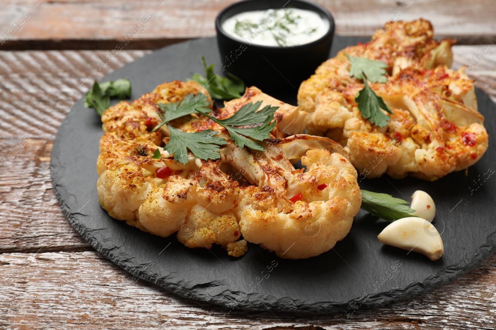 Photo of Delicious baked cauliflower steaks with sauce on wooden table, closeup