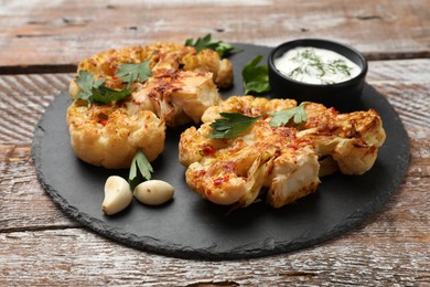 Photo of Delicious baked cauliflower steaks with sauce on wooden table, closeup