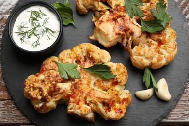 Photo of Delicious baked cauliflower steaks with sauce on wooden table, top view