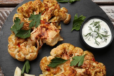 Photo of Delicious baked cauliflower steaks with sauce on wooden table, top view