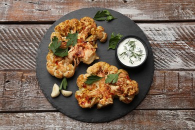 Photo of Delicious baked cauliflower steaks with sauce on wooden table, top view