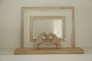 Blank picture frame with figure of hands on white shelf