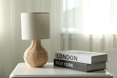 Books and lamp on nightstand near window indoors