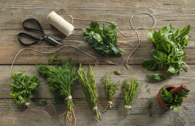 Different aromatic herbs, mortar with pestle, thread and scissors on wooden table, flat lay