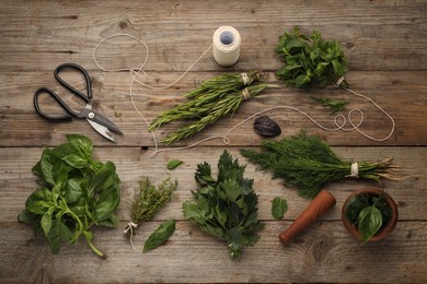 Photo of Different aromatic herbs, mortar with pestle, thread and scissors on wooden table, flat lay