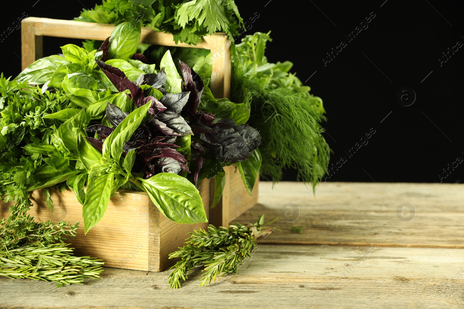 Photo of Different aromatic herbs in crate on wooden table against black background, space for text