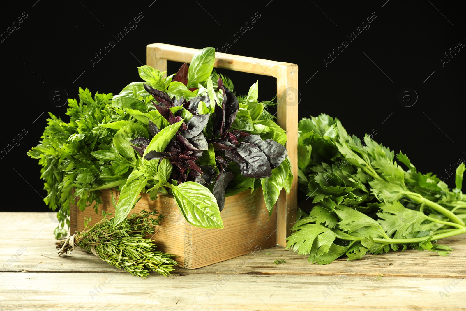 Photo of Different aromatic herbs in crate on wooden table against black background