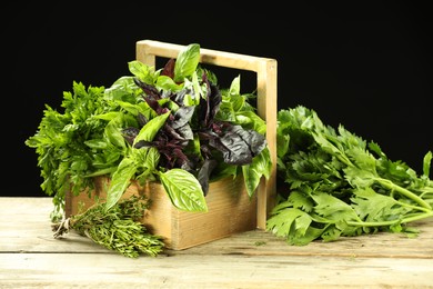 Photo of Different aromatic herbs in crate on wooden table against black background